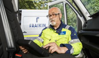 A Fraikin employee in a high-visibility jacket sits inside a vehicle cab, using a digital tablet.